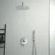 Duschbereich mit einer runden, modernen Regenbrause aus gebürstetem Edelstahl von Ideal Standard. Handbrause und Bedienelemente an der Wand montiert. Schwarze Ablage sichtbar.